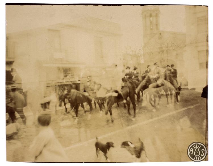 Genets a cavall desfilant per un carrer de Sabadell. Al fons el campanar de l'església de Sant Feliu.