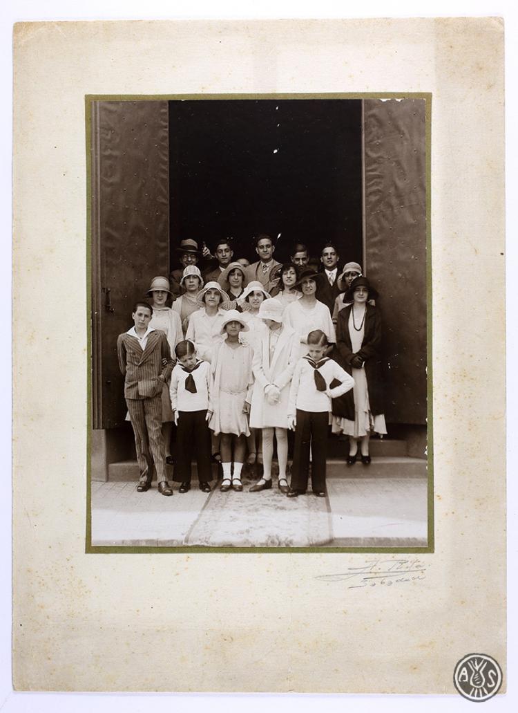 Retrat d'estudi d'una família vestida elegantment i infants vestits de primera comunió a la porta d'una església sesne identificar. Sabadell