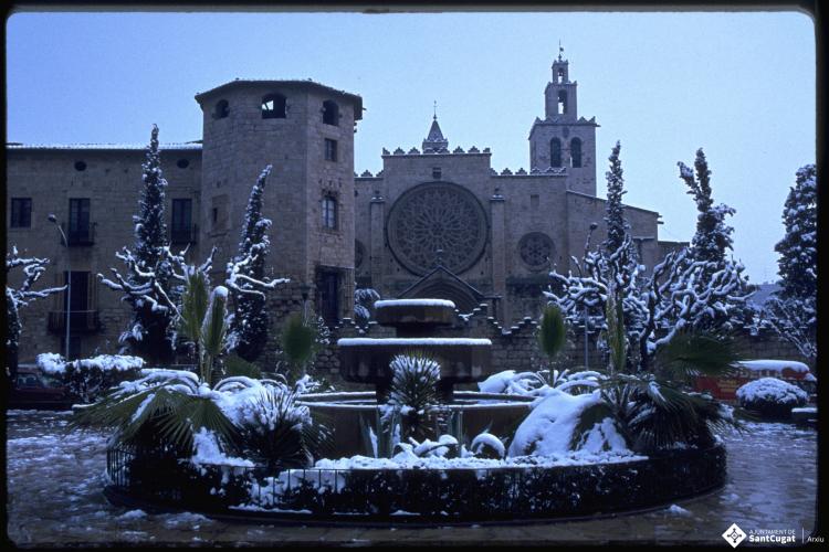 Font de la plaça d'Octavià coberta de neu, al fons, l'església de Sant Pere d'Octavià. 