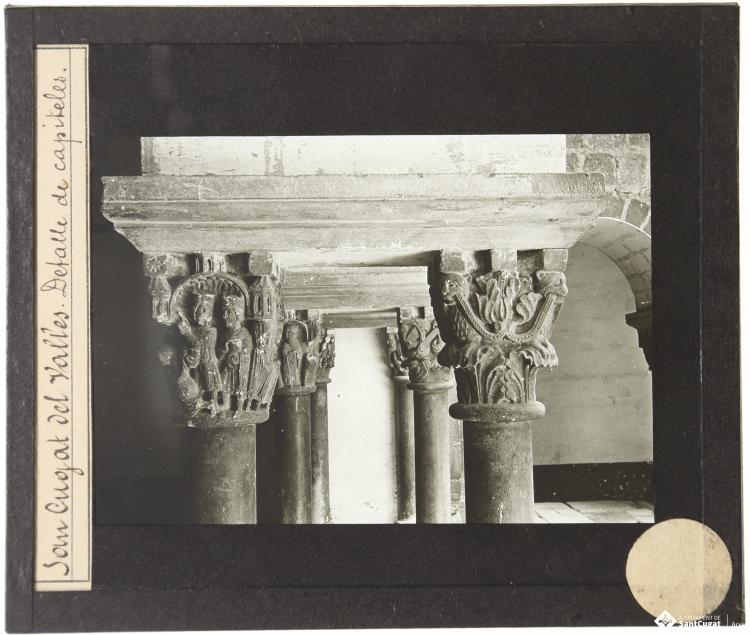 Parella de capitells, el capitell del cicle de la infància de Crist i un capitell amb representació vegetal, ala est del Claustre del Monestir de Sant Cugat del Vallès.