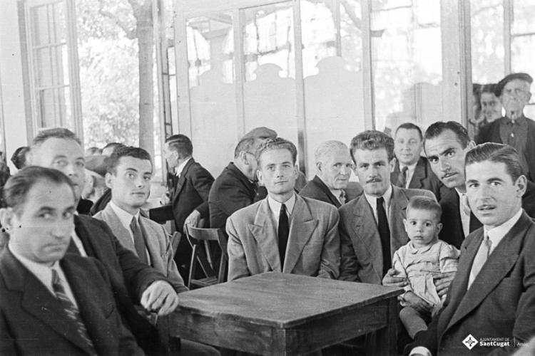 Actes de la festa inaugural de la restaurada Societat Coral La Unió Santcugatenca. Jaume Grau assegut amb un grup d'homes i un infant, a la sala del cafè de la Unió.