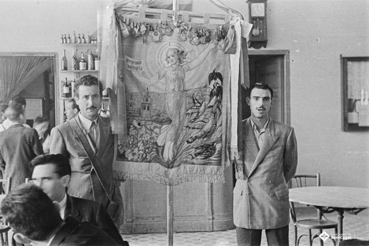 Actes de la festa inaugural de la restaurada Societat Coral La Unió Santcugatenca. Pere Rifé i un altre home retratats amb l'estendard a la sala del cafè de la Unió.