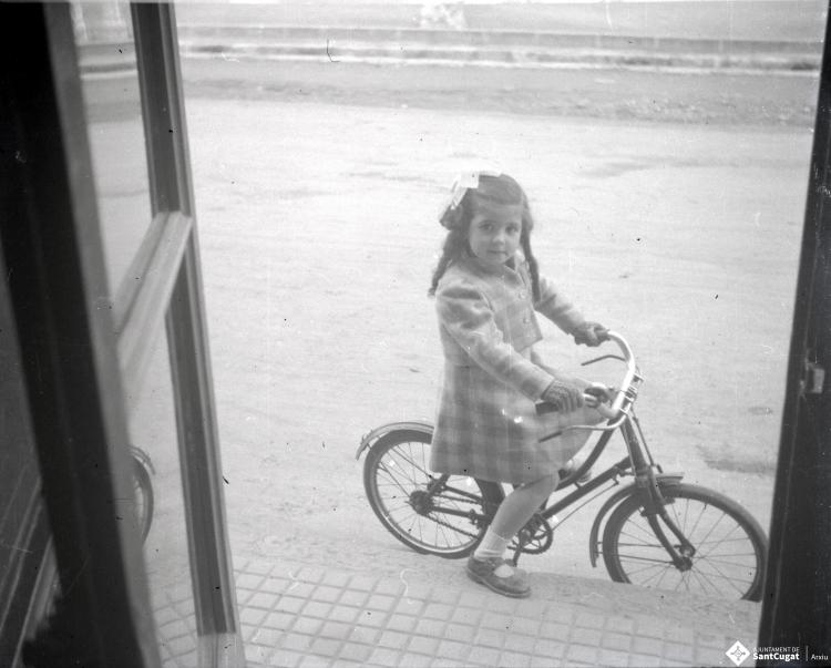 Elisabet Cabanas en bicicleta davant de la porta de la botiga de Cal Cabanas.