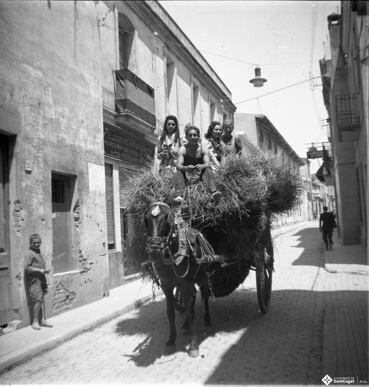 Carro carregat de palla amb gent al damunt circulant pel carrer de Santa Maria.