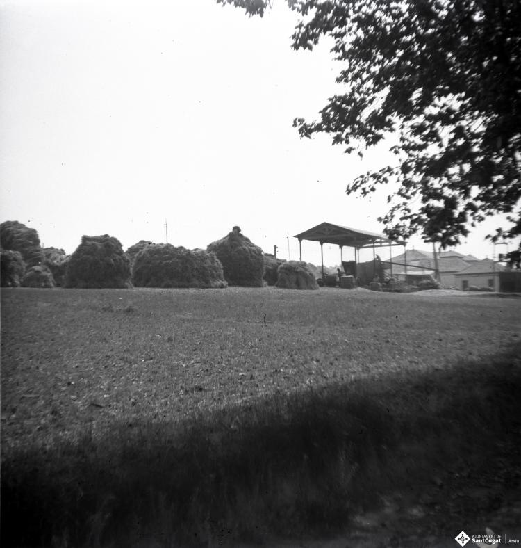 Homes prop d'un cobert on hi ha una màquina de batre, al camp de Can Mates.