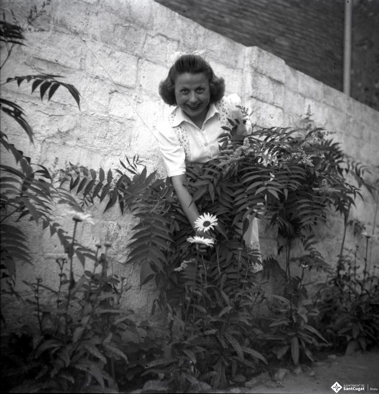 Dona retratada, mostrant una flor, al pati del fotògraf.