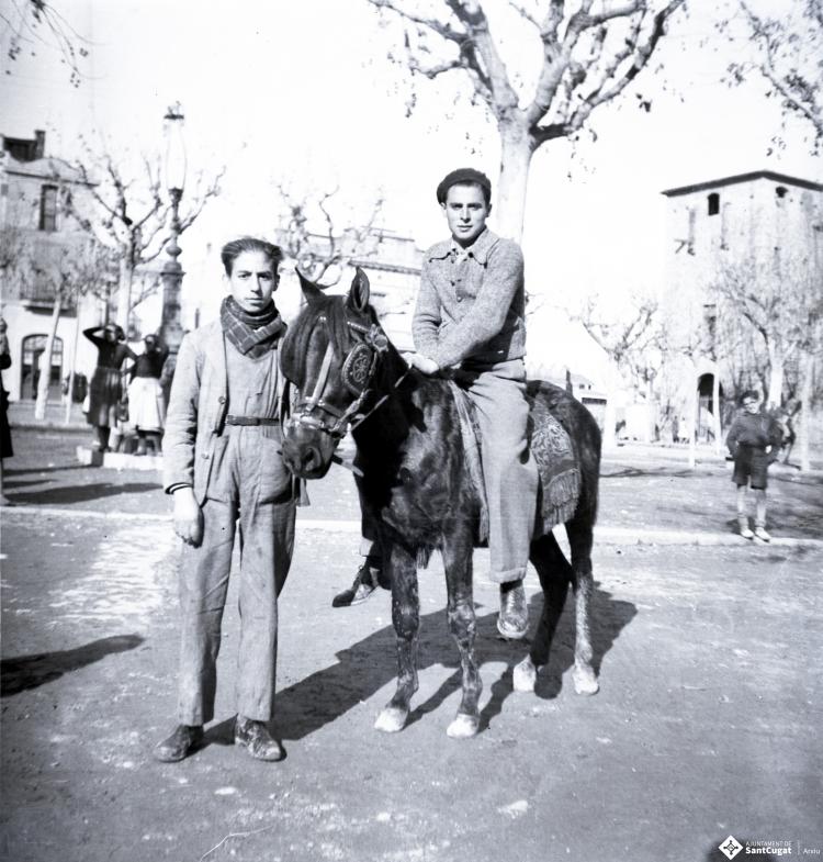 Tres Tombs, retrat de dos nois, un d'ells muntant un ruc, a la plaça d'Octavià.
