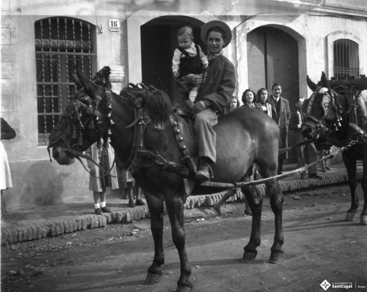 Festa de Sant Antoni Abat. Retrat d'un home muntant amb un infant en braços al seu pas per la plaça de Barcelona.