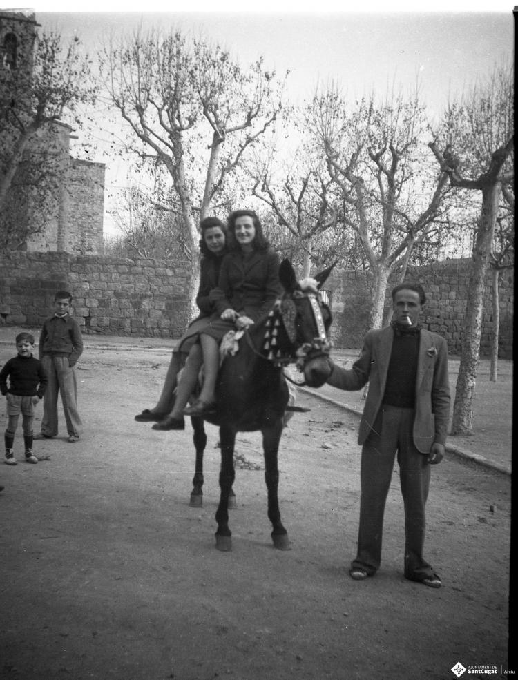 Festa de Sant Antoni Abat. Retrat de dues noies joves muntant un cavall portat per un home, al fons Cal Boter Negre, a la plaça d'Octavià.