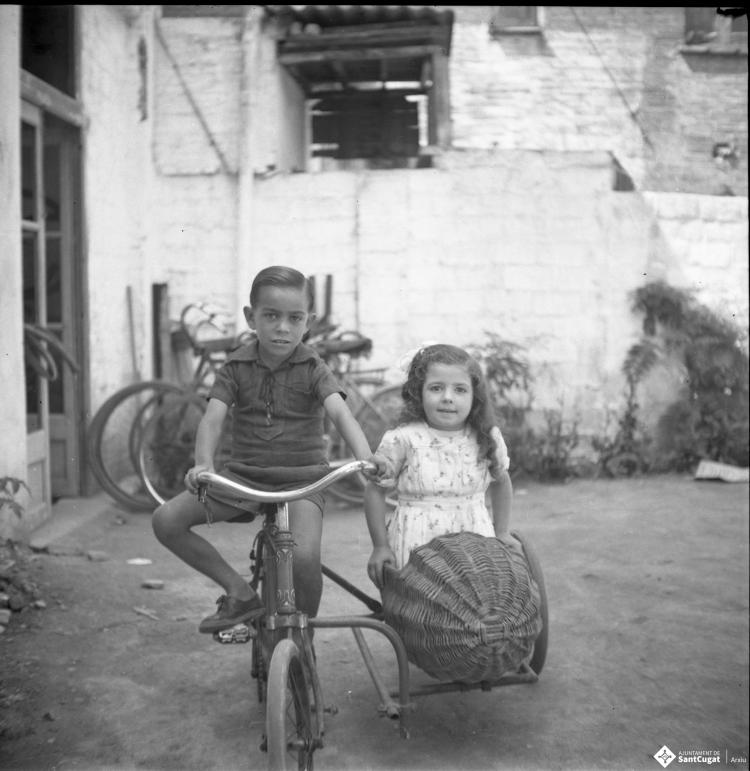 Retrat d'un infant en bicicleta i de l'Elisabet asseguda en el sidecar de vímet d'aquesta.