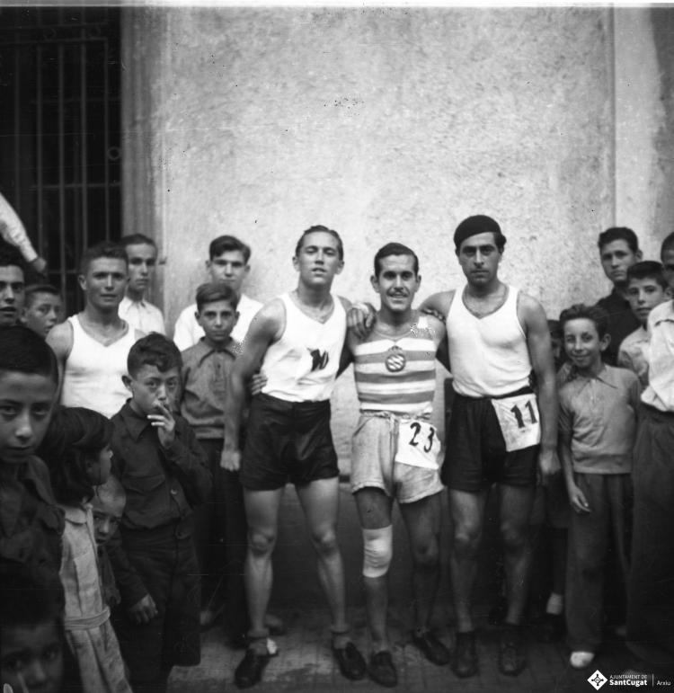Cursa popular de la Festa Major, retrat dels corredors amb el dorsal 10, 23 i 11. El corredor amb el dorsal 23 du un equipament esportiu que recorda el de la Secció d'atletisme del RCD Espanyol.