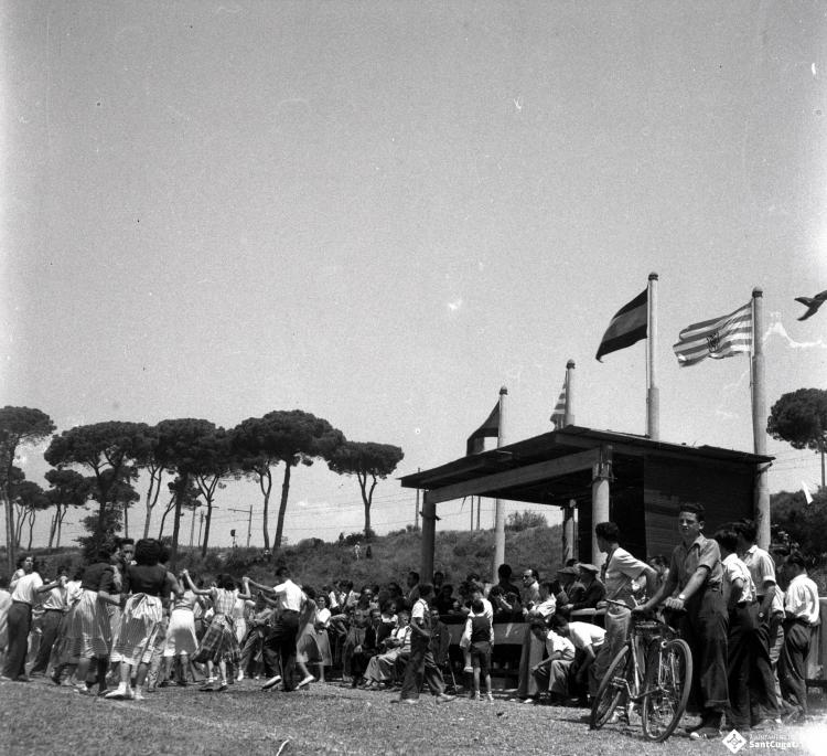 Activitats festives, sardanes. Ubicació no identificada, a prop hi ha una catenària d'un tren.