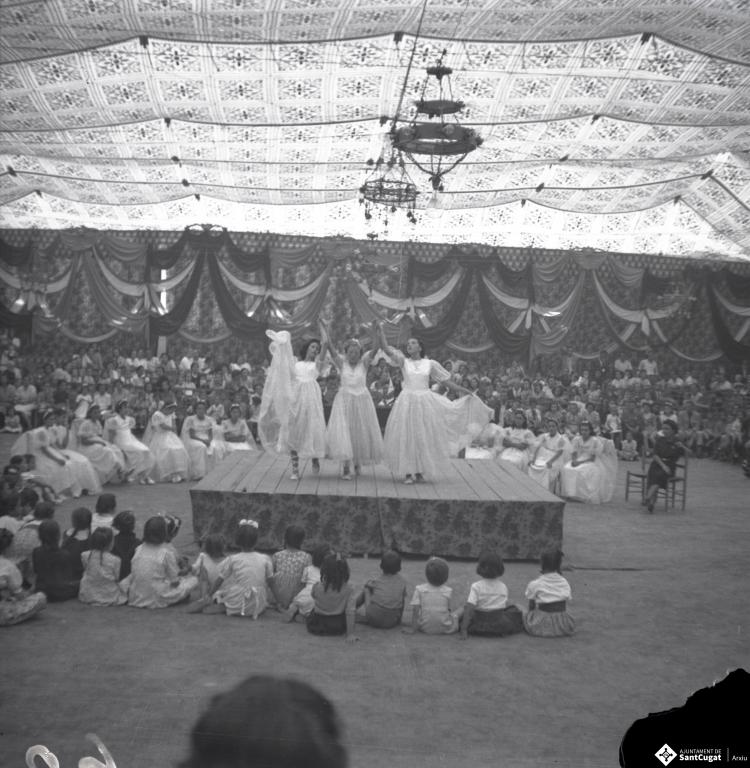 Festa Major. Noies ballant a l'escenari de l'envelat, probablement de la secció infantil de l'Esbart Dansaire, acompanyades per  Manuel Farrés i dues dones uniformades.