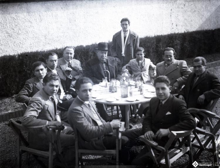 Celebració davant de la seu de la Falange a Cal Barbany. Retrat d'un grup d'homes en una de les taules del quiosc de begudes de la plaça del Quatre Cantons.