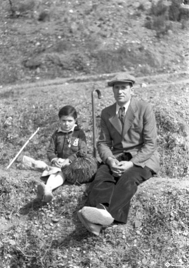 Aplec de Sant Medir. Retrat d'una nena i un home asseguts a terra.