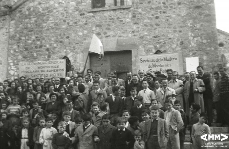 Grup de persones a les escales de l'església amb una bandera
