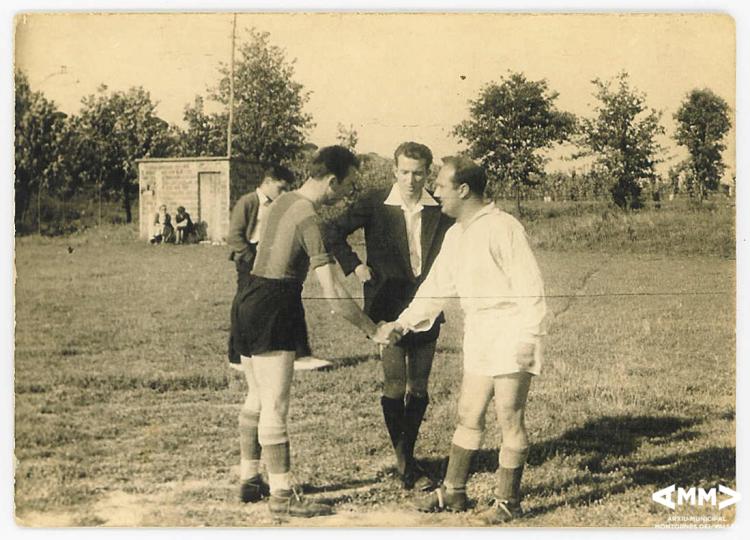 Dos jugadors de futbol es saluden davant de la presència de l'àrbitre del partit