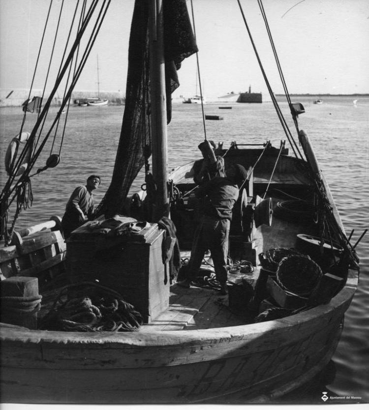 Tres pescadors hissant la vela d'una barca de pesca