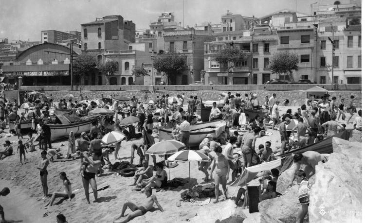 Platja plena de banyistes entre les barques varades a la sorra