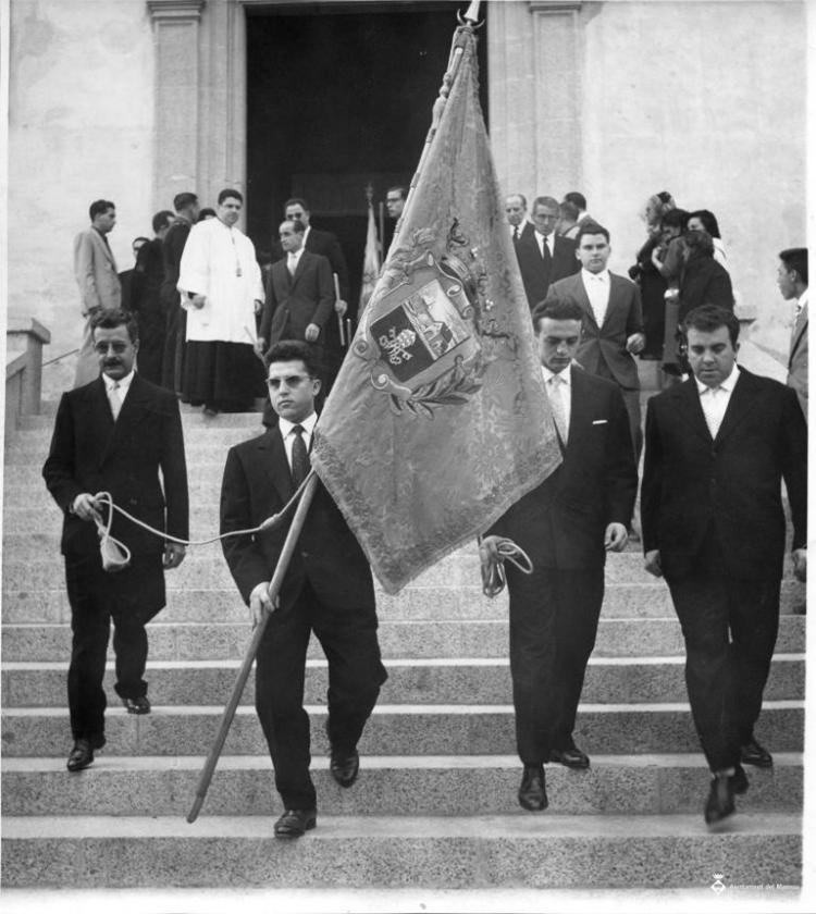 Homes amb la bandera de l'Ajuntament baixant les escales de l'església per Corpus