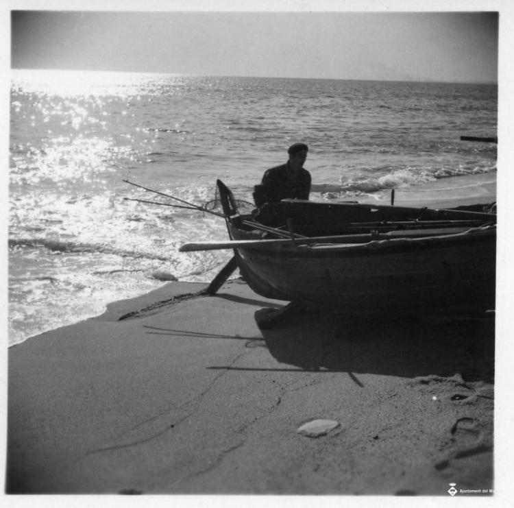 Pescador varant una barca de rems a la platja del Masnou
