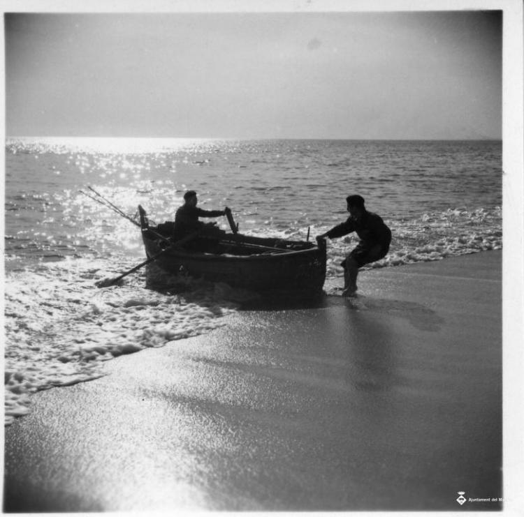 Dos homes varant una barca a la platja del Masnou
