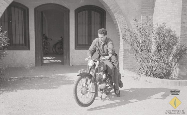 Joan Pi Tintoré a sobre d'una motocicleta Montesa Impala davant la façana de les caves Rondel a Cervelló