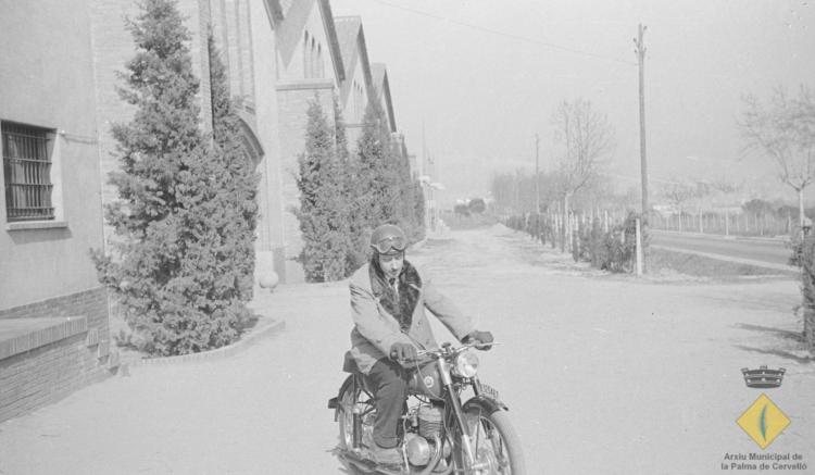 Josep Noguero Roca amb una motocicleta Montesa Impala davant la façana de les caves Rondel de Cervelló amb la carretera N-340 a la dreta