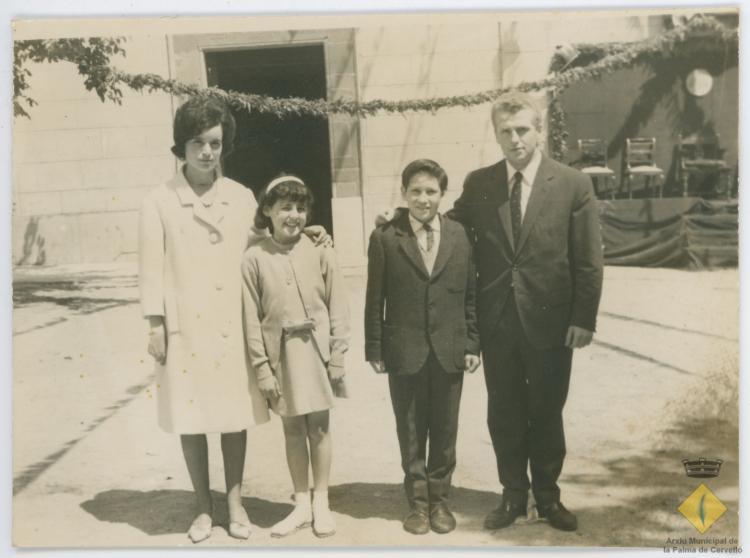 Els nens Rosa Maria Giberga i Josep Busquet Costabella amb els seus padrins, Rosa Albertí i Antonio Busquet, el dia de la seva confirmació, a la plaça de l'església decorada per la visita del bisbe Jubany