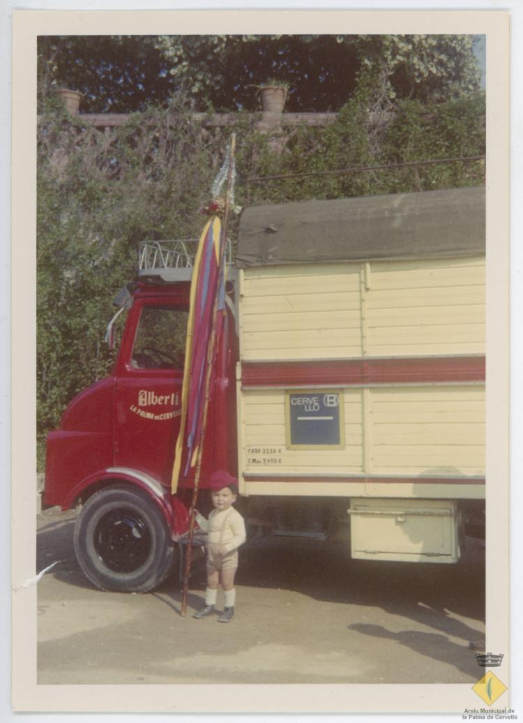 El nen Jordi Busquet Albertí amb vestit tradicional i un penó a ca n'Iglésies davant un dels camions de l'empresa Albertí