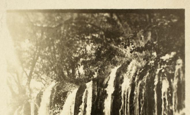 Retrat de dona sobre un pont de fusta amb un salt d'aigua al fons. S.l.