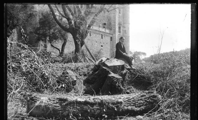 Home assegut sobre un arbre talat del bosc de Can Feu amb la façana posterior del castell al fons. Sabadell