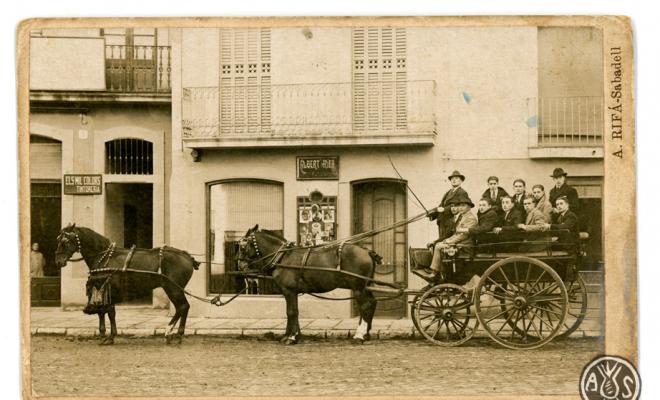 Carro a la plaça Marquilles, davant de la botiga del fotògraf Albert Rifà. Sabadell. Edició postal.