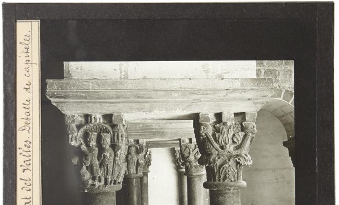 Parella de capitells, el capitell del cicle de la infància de Crist i un capitell amb representació vegetal, ala est del Claustre del Monestir de Sant Cugat del Vallès.