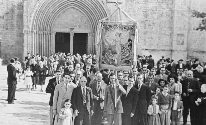 Actes de la festa inaugural de la restaurada Societat Coral La Unió Santcugatenca. Pere Rifé portant l'estendard de la Unió encapçala un grup de gent a la sortida de missa, a la llotgeta del Monestir.