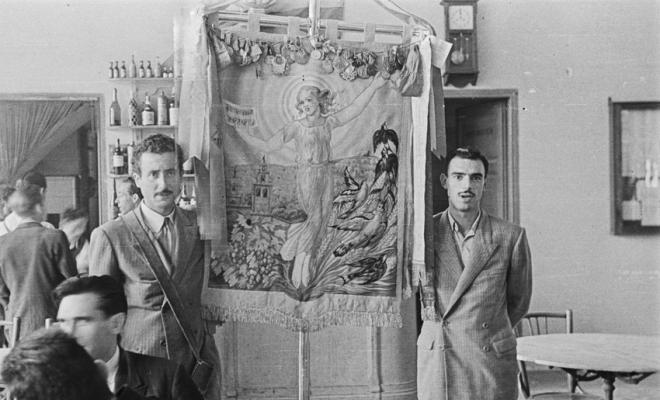 Actes de la festa inaugural de la restaurada Societat Coral La Unió Santcugatenca. Pere Rifé i un altre home retratats amb l'estendard a la sala del cafè de la Unió.
