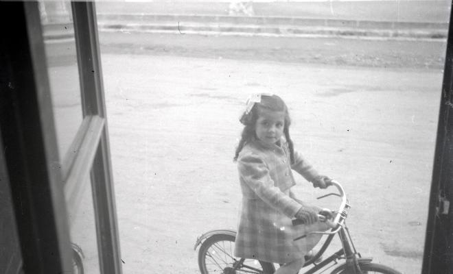 Elisabet Cabanas en bicicleta davant de la porta de la botiga de Cal Cabanas.