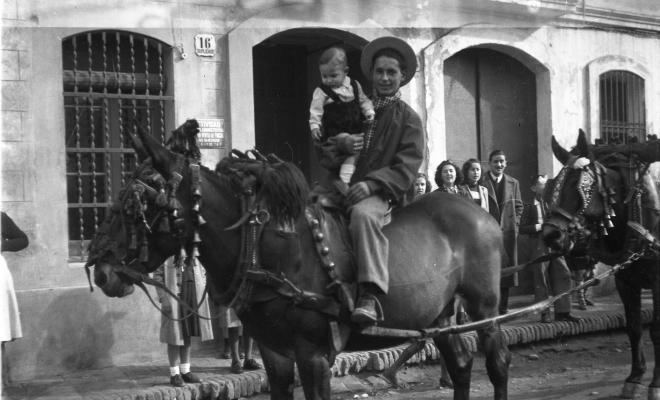 Festa de Sant Antoni Abat. Retrat d'un home muntant amb un infant en braços al seu pas per la plaça de Barcelona.