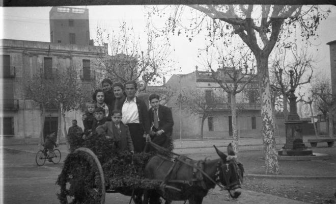 Festa de Sant Antoni Abat. Retrat d'un grup de persones en un carro guarnit,  just davant del brollador de benzina de la plaça d'Octavià. Al fons de la imatge és veu l'edifici de Cal Boter Negre.