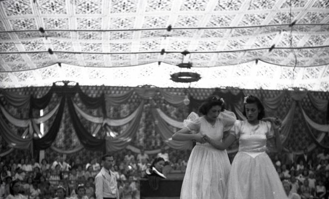 Festa Major. Noies ballant a l'escenari de l'envelat, probablement de la secció infantil de l'Esbart Dansaire, acompanyades per  Manuel Farrés i dues dones uniformades.