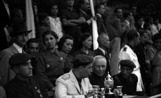 Festa Major. Autoritats assegudes darrere una taula amb copes i trofeus, presideixen l'acte, el governador civil i Antonio Federico Correa Véglison, mossèn Griera,  i Nicolau Villar Recio.