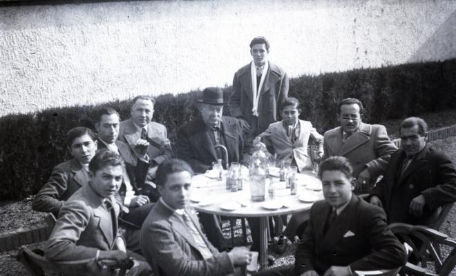 Celebració davant de la seu de la Falange a Cal Barbany. Retrat d'un grup d'homes en una de les taules del quiosc de begudes de la plaça del Quatre Cantons.