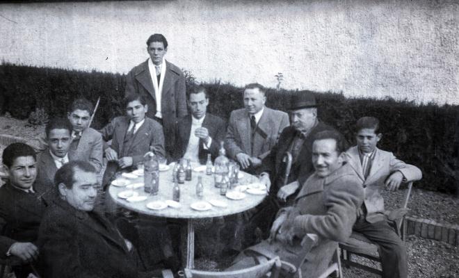 Celebració davant de la seu de la Falange a Cal Barbany. Retrat d'un grup d'homes en una de les taules del quiosc de begudes de la plaça del Quatre Cantons.