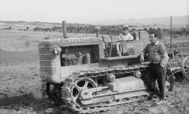 Retrat d'un home i un infant assegut en un tractor en un camp.