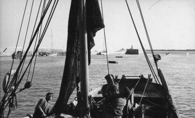 Tres pescadors hissant la vela d'una barca de pesca