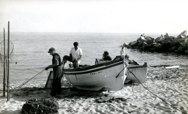Pescadors arreglant les xarxes al costat de les barques a la platja