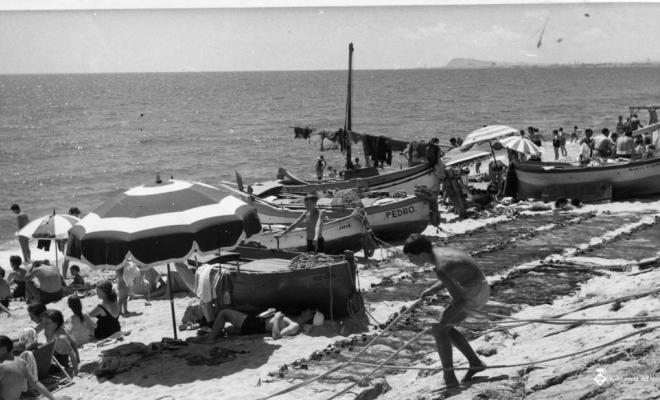 Banyistes prenent el sol entre les barques i les xarxes de pesca
