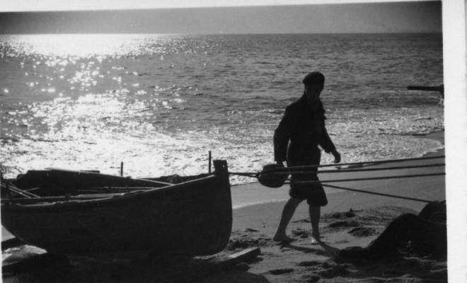 Un home caminant al costat d'una barca de pesca que s'està varant a la platja