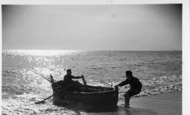 Dos homes varant una barca a la platja del Masnou