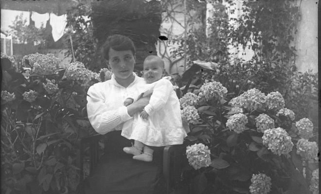 Retrat d'una dona amb un nadó en braços al jardí d'una casa